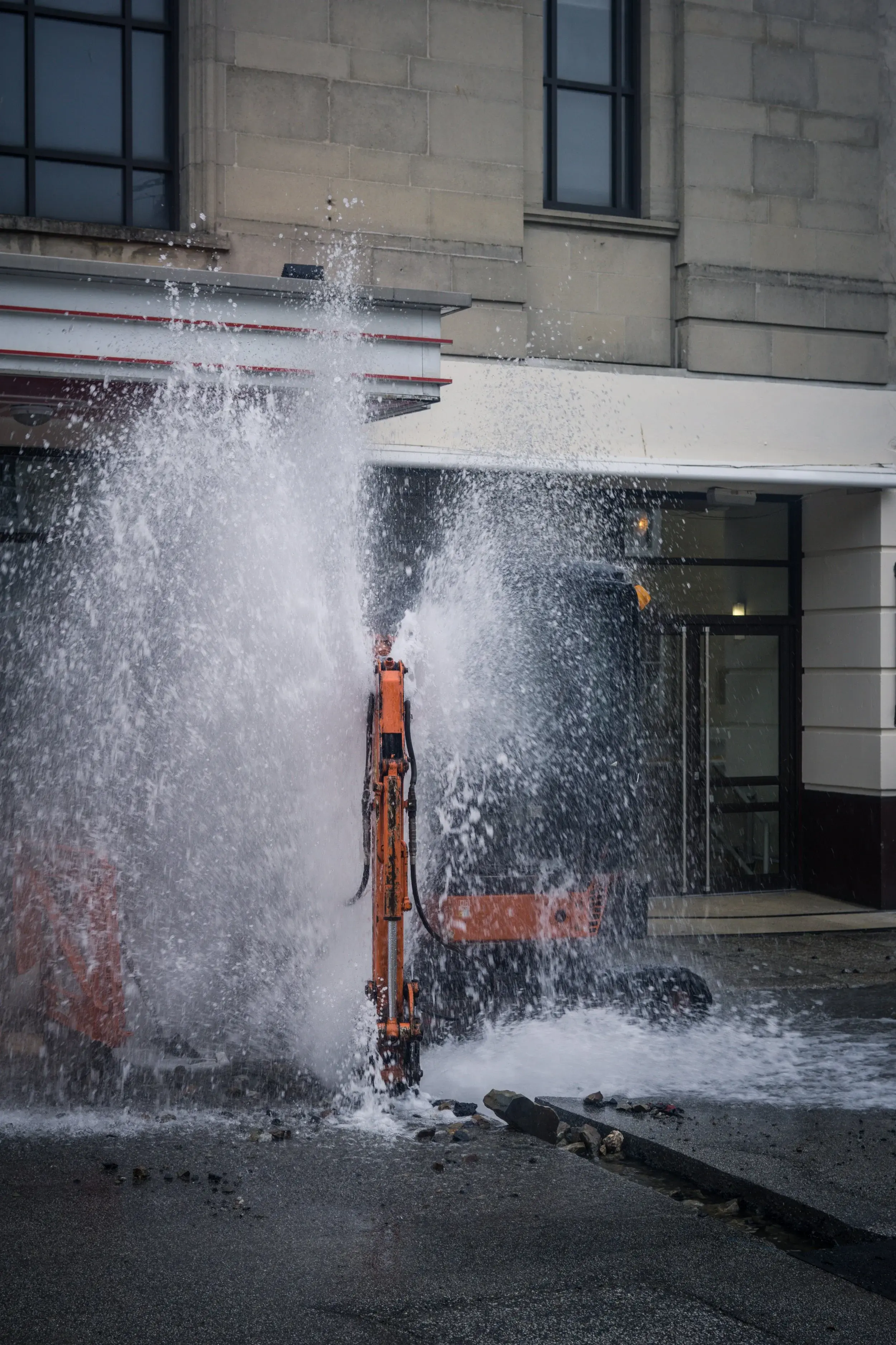 An orange street cleaning machine spraying water in front of a modern building.